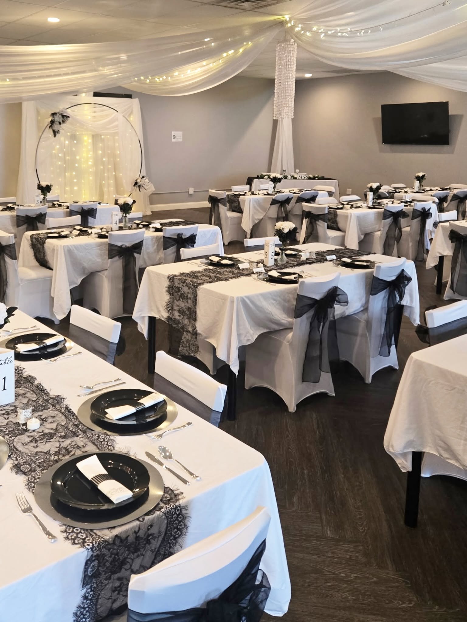 Hall set with white-draped tables, black lace runners and chairs tied with black sashes